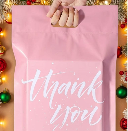 Pink bag with 'thank you' text held by a hand, surrounded by Christmas decorations.