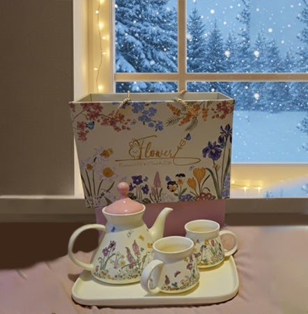 Tea set with floral design on a tray in front of a window with snowy scenery.