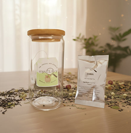 Glass jar with wooden lid and tea packaging on a wooden surface with loose tea leaves.